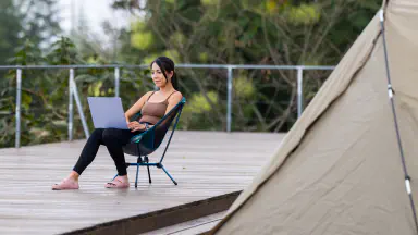 Woman working on laptop outside a tent.